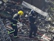 Cảnh sát che chắn cho lính cứu hỏa trong lúc bước qua những mảnh vỡ la liệt tại sân chung cư Grenfell. Ảnh:AP