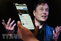 Tài khoản Twitter của tỷ phú Elon Musk trên màn hình điện thoại và ảnh chụp ông Musk (phía sau) tại một sự kiện ở Washington, DC, Mỹ ngày 14/4/2022. (Ảnh: AFP/TTXVN).