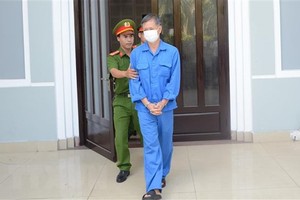 Cơ quan chức năng dẫn giải cựu Giám đốc CDC Đà Nẵng ra xe sau khi kết thúc phiên tòa sáng 25/8. (Ảnh: Văn Dũng/TTXVN)