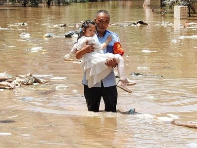 Sơ tán trẻ em khỏi khu vực bị ngập do mưa lũ. (Ảnh: AFP/TTXVN).