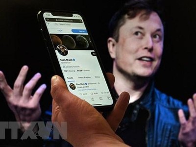 Tài khoản Twitter của tỷ phú Elon Musk trên màn hình điện thoại và ảnh chụp ông Musk (phía sau) tại một sự kiện ở Washington, DC, Mỹ ngày 14/4/2022. (Ảnh: AFP/TTXVN)