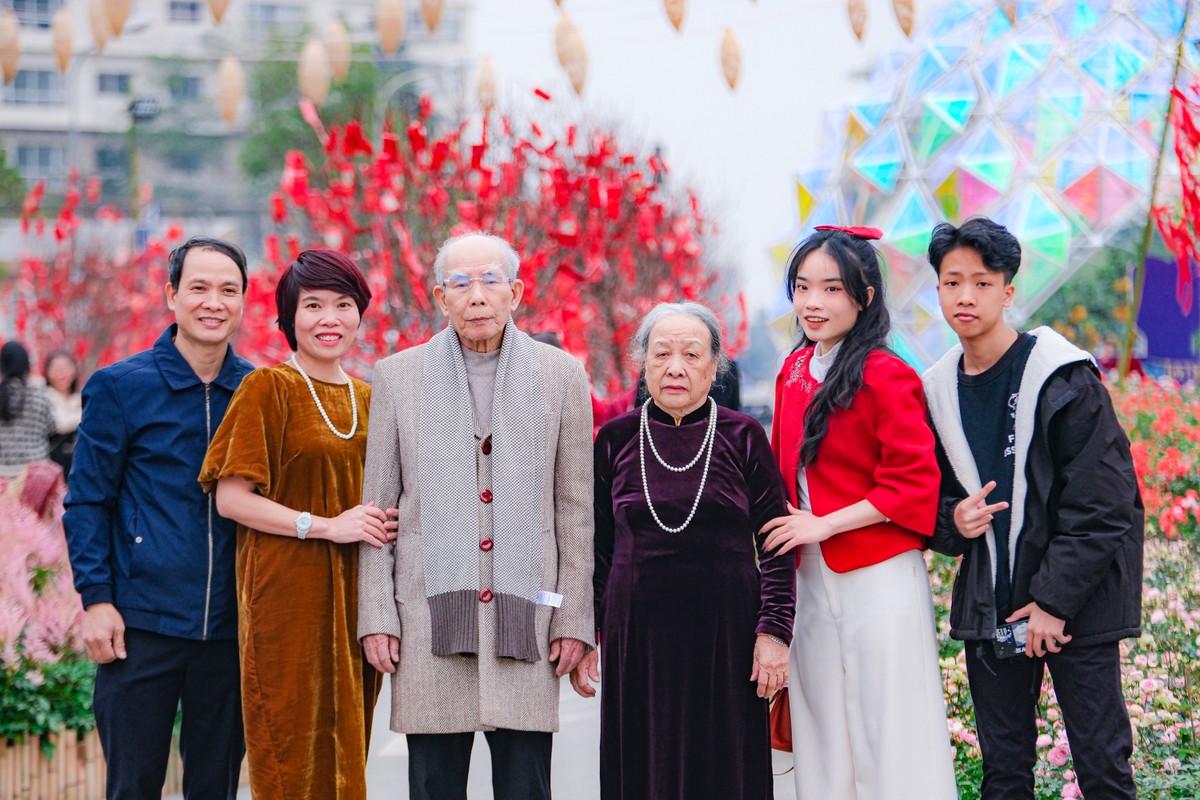 Người dân xúng xính diện áo dài cùng gia đình, người thân đến ngắm hoa, chụp ảnh. Khu vực cây tài lộc nằm ở vị trí trung tâm, nổi bật với những mảnh lụa đỏ rực rỡ.