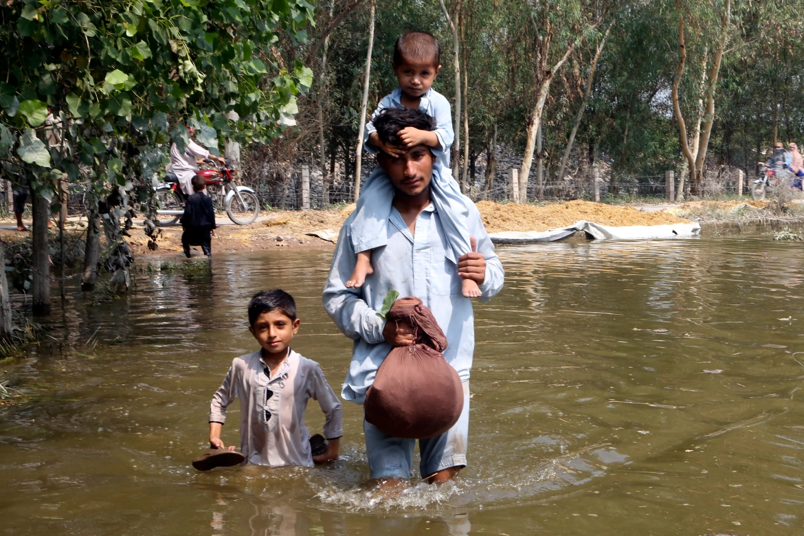 Một người đàn ông bế con trai khi lội qua dòng nước lũ ở Charsadda thuộc tỉnh Khyber Pakhtunkhwa của Pakistan